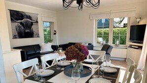 A dining area with a round table set for six, white chairs, and a vase with flowers. - 6-person Holiday Home With Garden (Sint Maartensvlotbrug)