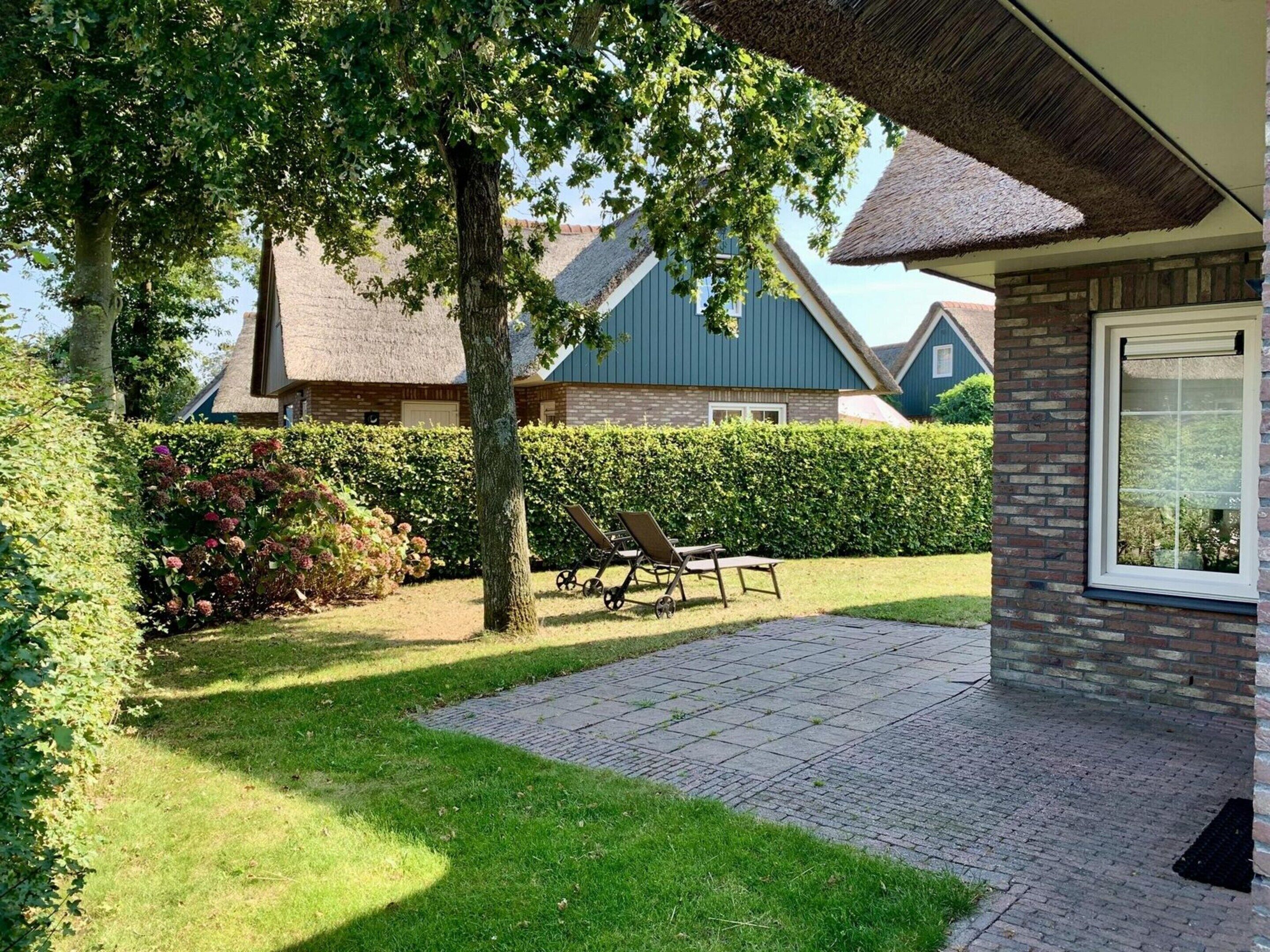 Ein Wohnhaus mit gepflasterter Terrasse, Rasen und einem Haus mit Strohdach.