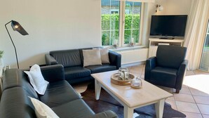 A modern living room with a sectional sofa, a single armchair, a coffee table, and a TV. - 6-person Holiday Home With Garden (Sint Maartensvlotbrug)