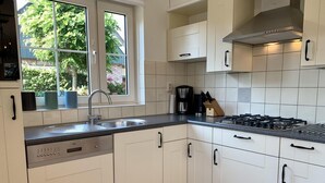 A modern kitchen with white cabinets, a built-in dishwasher, a gas stove, and a window overlooking a garden. - 6-person Holiday Home With Garden (Sint Maartensvlotbrug)