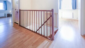 Amplia habitación con suelo de madera, barandilla de madera y vistas a una ventana con cortinas.