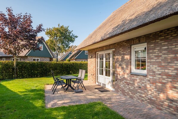 A brick house with a thatched roof, a patio with a table and chairs, and a well-maintained garden. - Pleasant Villa Near sea and Beach (Sint Maartensvlotbrug)