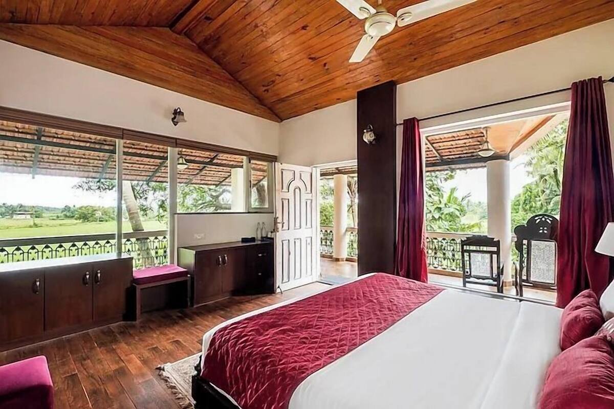 A bedroom with a large bed, wooden ceiling, and a view of a garden.
