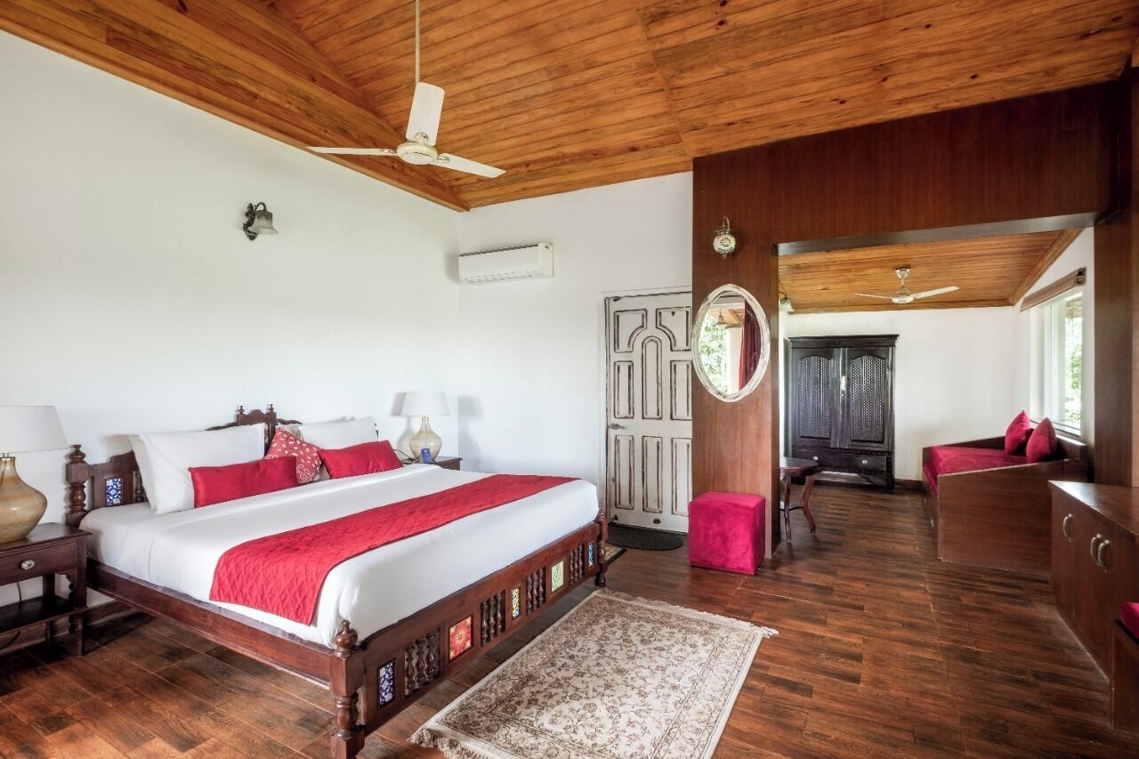 A spacious bedroom with a large bed, wooden ceiling, and a small sitting area with a red chair.