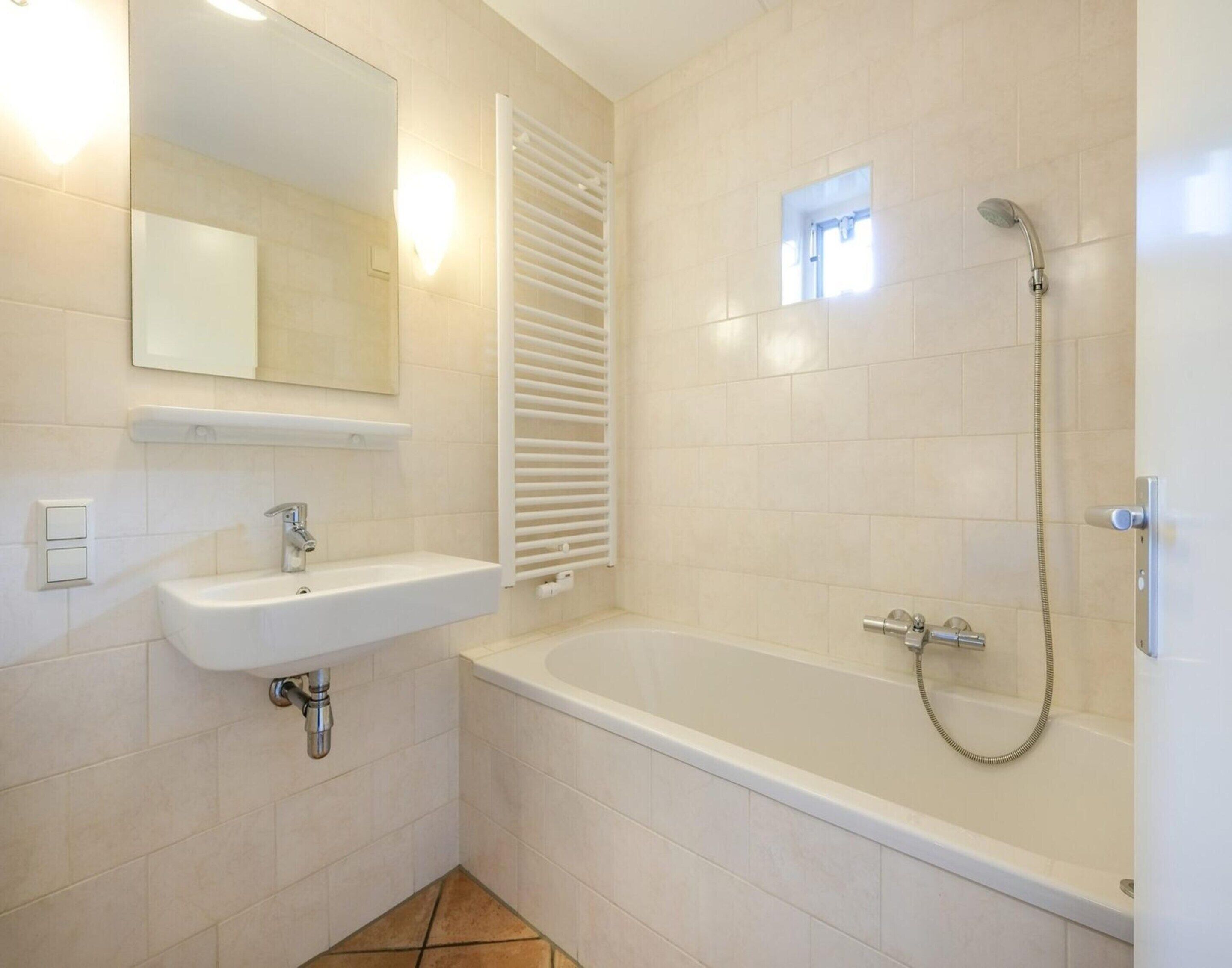 A bathroom with a white sink, mirror, and bathtub with a shower head.