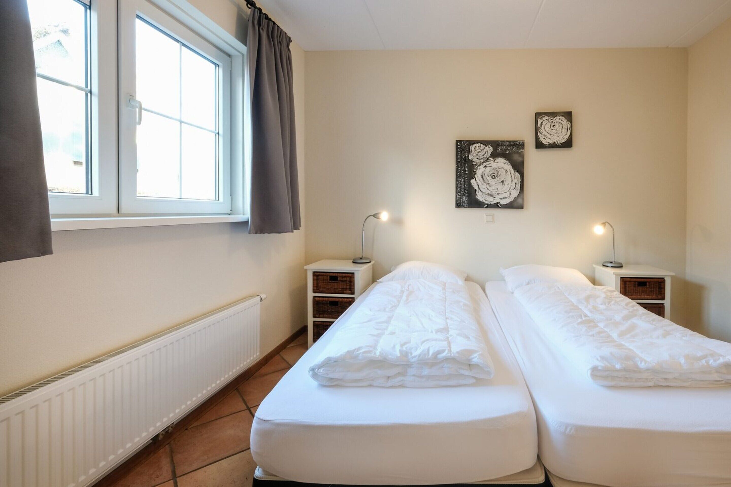 A room with two single beds, a radiator, a window with curtains, and two wall-mounted lamps.