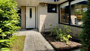 A modern house with a brick exterior, a white door, and a window overlooking a garden.