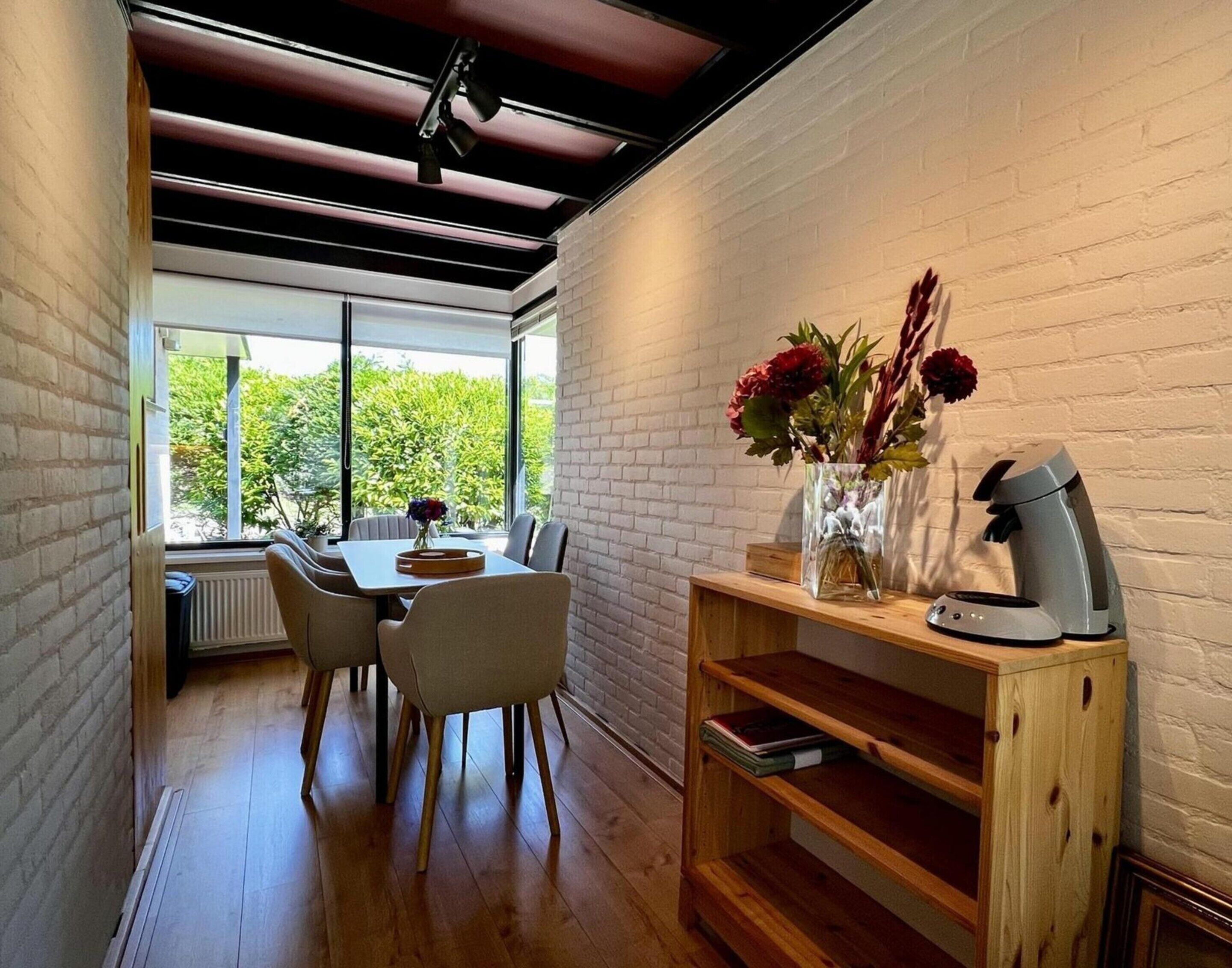 A dining area with a table, chairs, a coffee machine, and a vase with flowers.