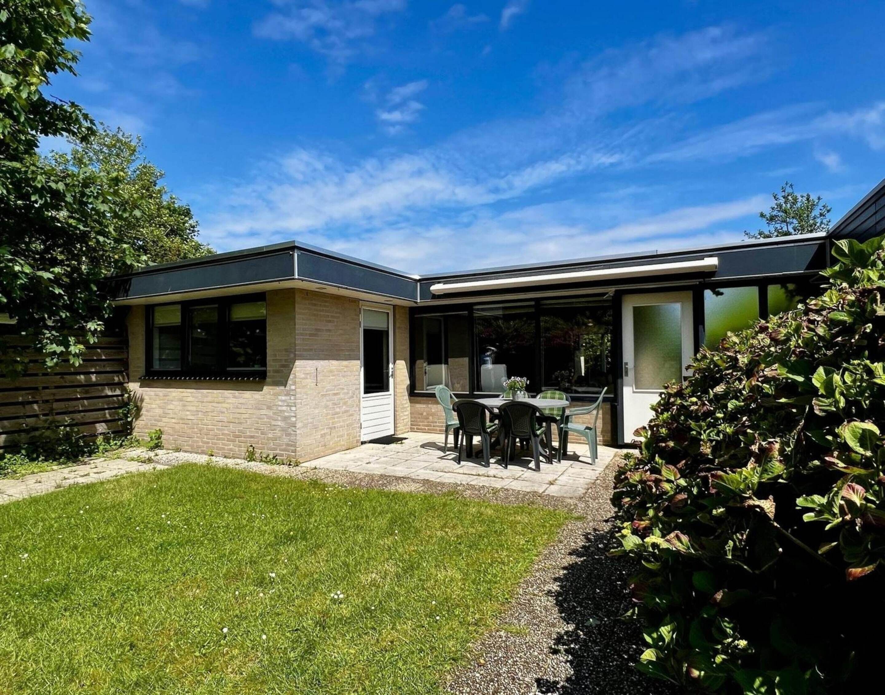 A modern house with a patio, a brick exterior, and a glass door leading to a covered outdoor area.