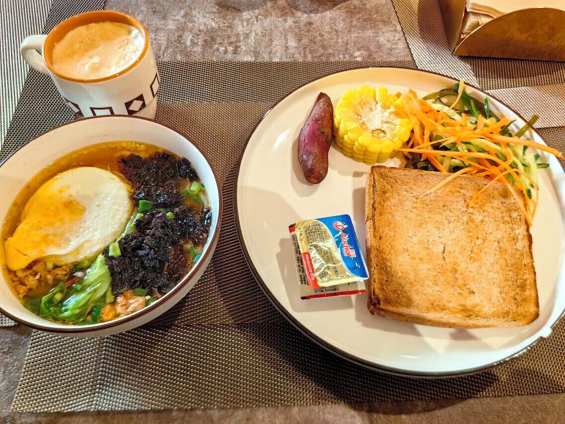 A meal consisting of a bowl of soup with vegetables and a slice of toast, a cup of coffee, and a plate with a sweet potato, corn, and a salad.