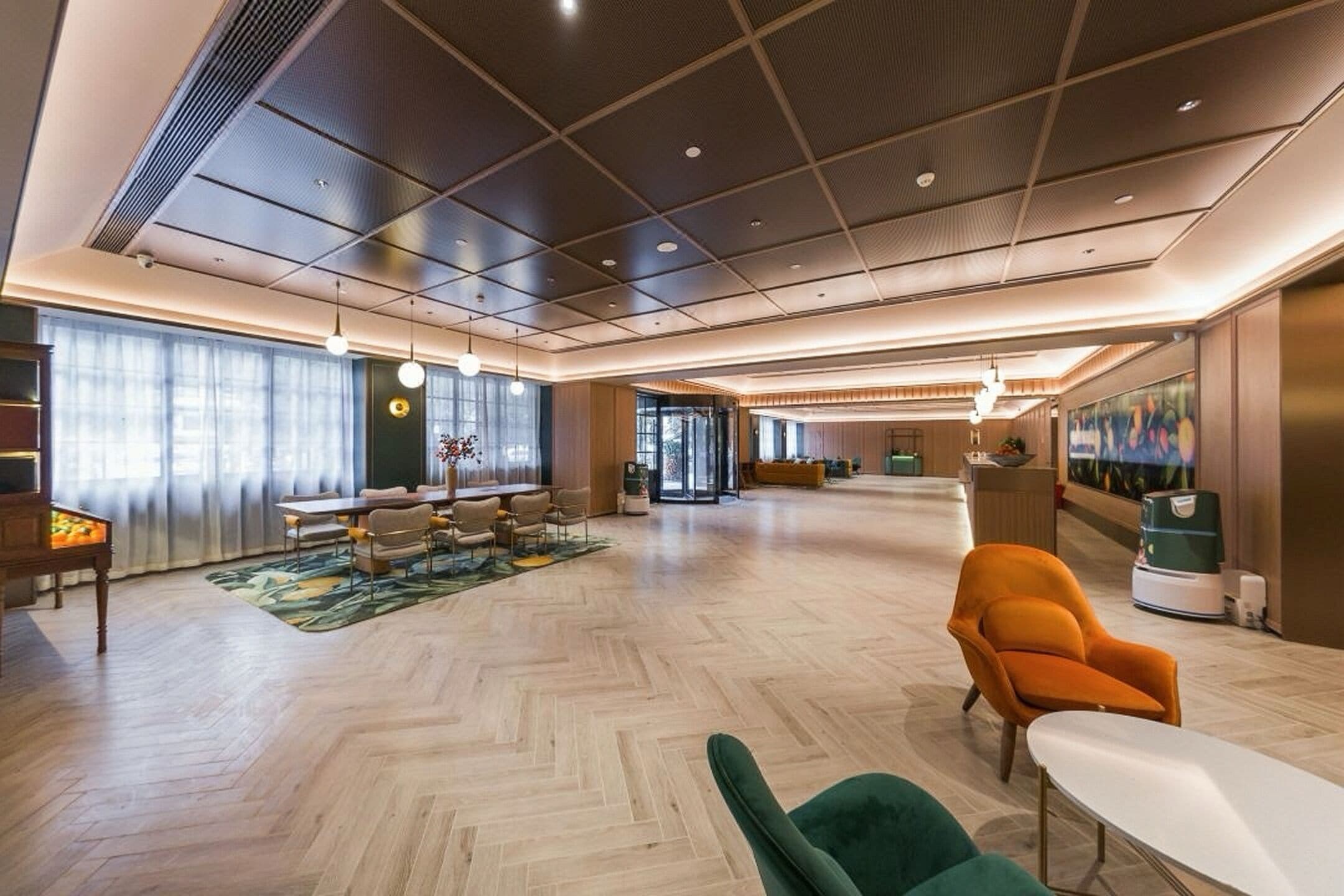 Eine geräumige Lobby mit Fischgrätparkettboden, einem Empfangstresen und einer Sitzecke mit Stühlen und einer Couch.