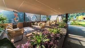 Un área de descanso moderna al aire libre con asientos y jardineras, amplias ventanas que ofrecen vistas del paisaje circundante.