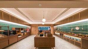 Un amplio vestíbulo de hotel con un mostrador de recepción de madera en el centro, paredes con azulejos verdes y un suelo con diseño de espiga.