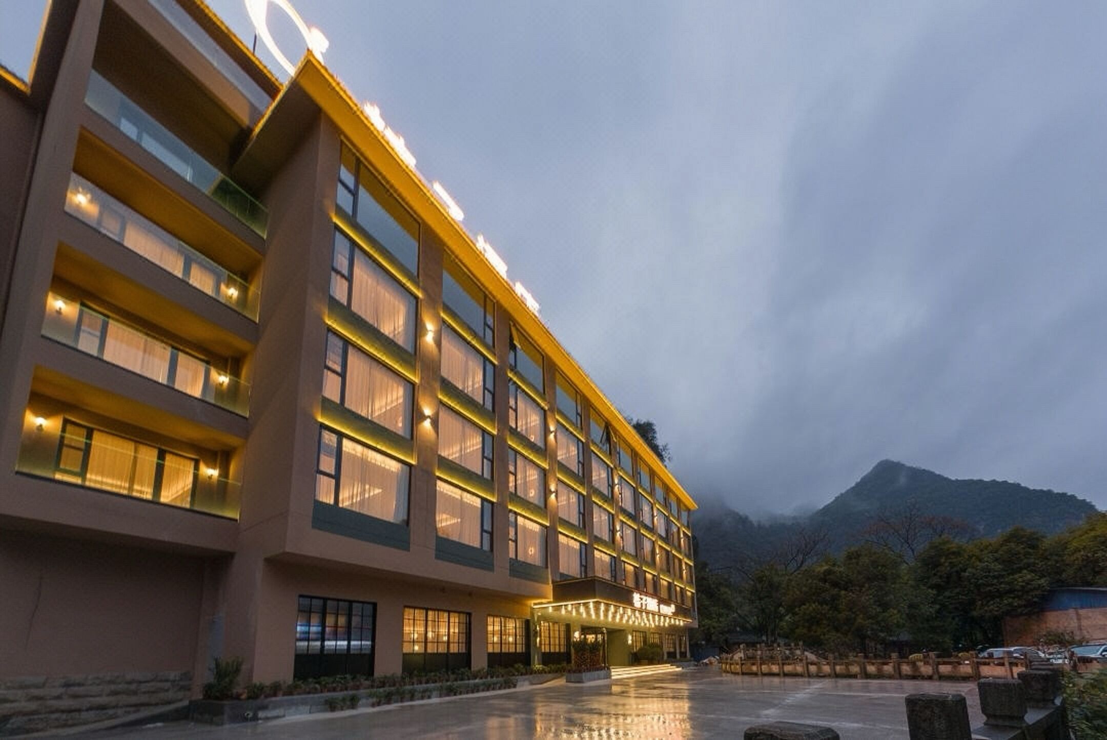 Un hôtel à plusieurs étages au design moderne, doté d’une entrée imposante et offrant une vue sur les montagnes en arrière-plan.