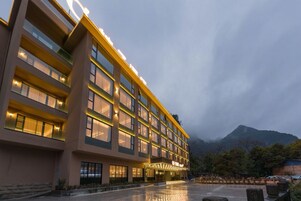 Un hotel de varios pisos con diseño moderno, destacándose su entrada principal y mostrando vistas de montañas al fondo.
