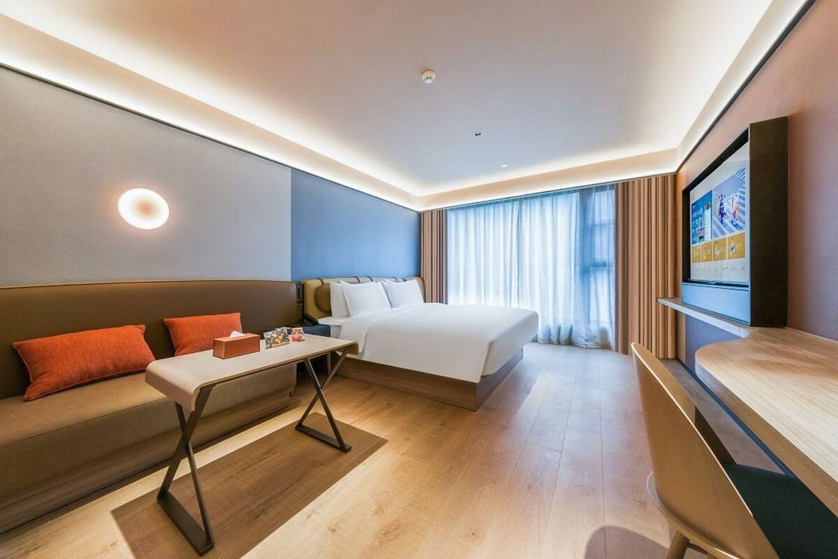 Una habitación de hotel moderna con una cama, un sofá, una mesita y un televisor.