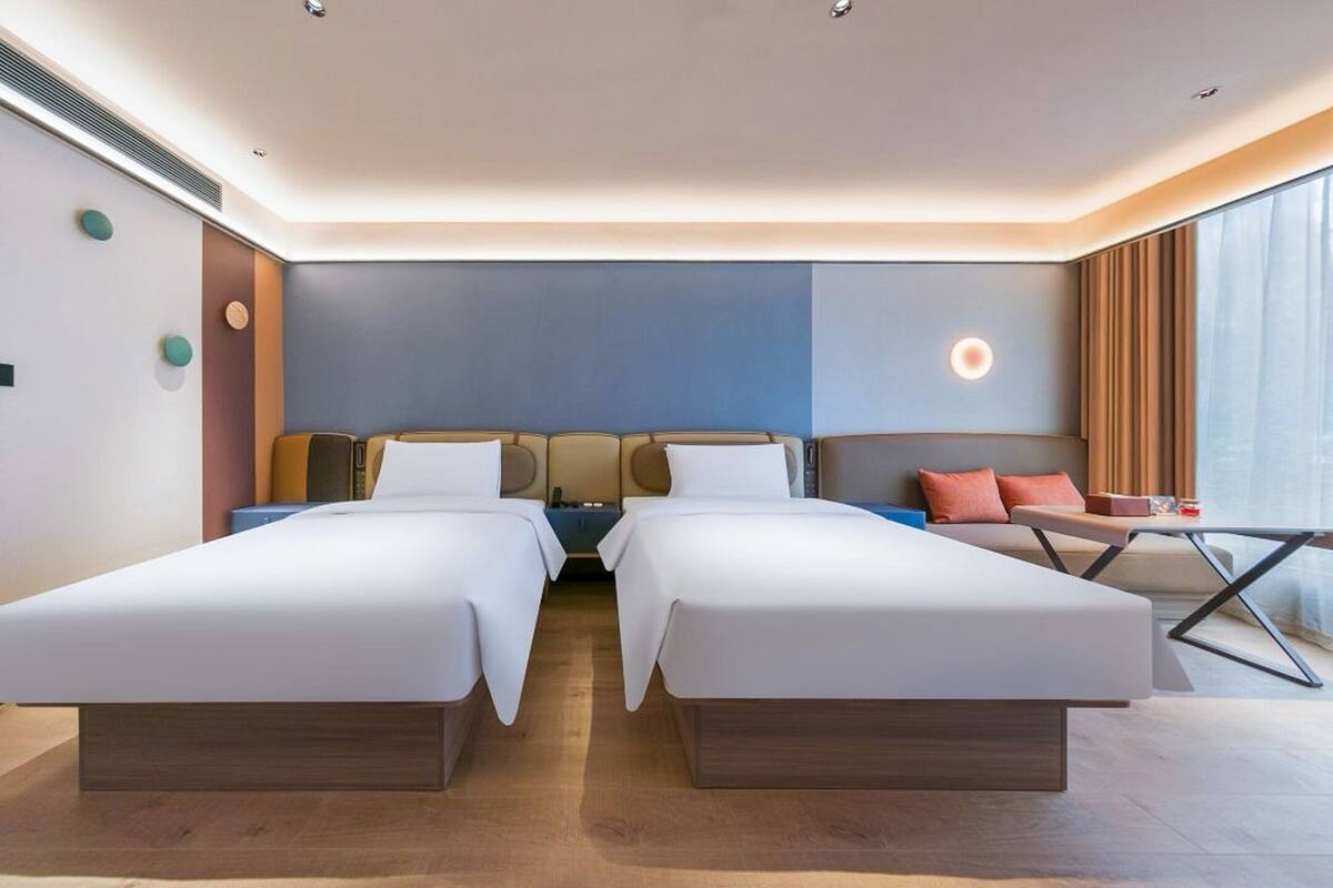 Una habitación de hotel moderna con dos camas individuales, una mesita y un sofá.