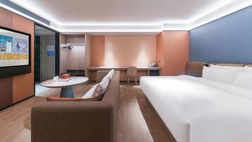 Una habitación de hotel moderna con una cama grande, un sofá, un escritorio y una pantalla de televisión que muestra un canal deportivo.