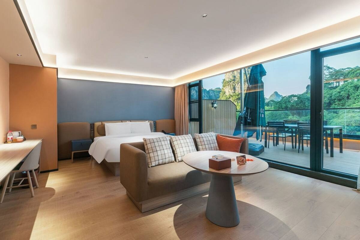 Habitación de hotel moderna con sofá, una mesita, escritorio y balcón con mobiliario exterior.
