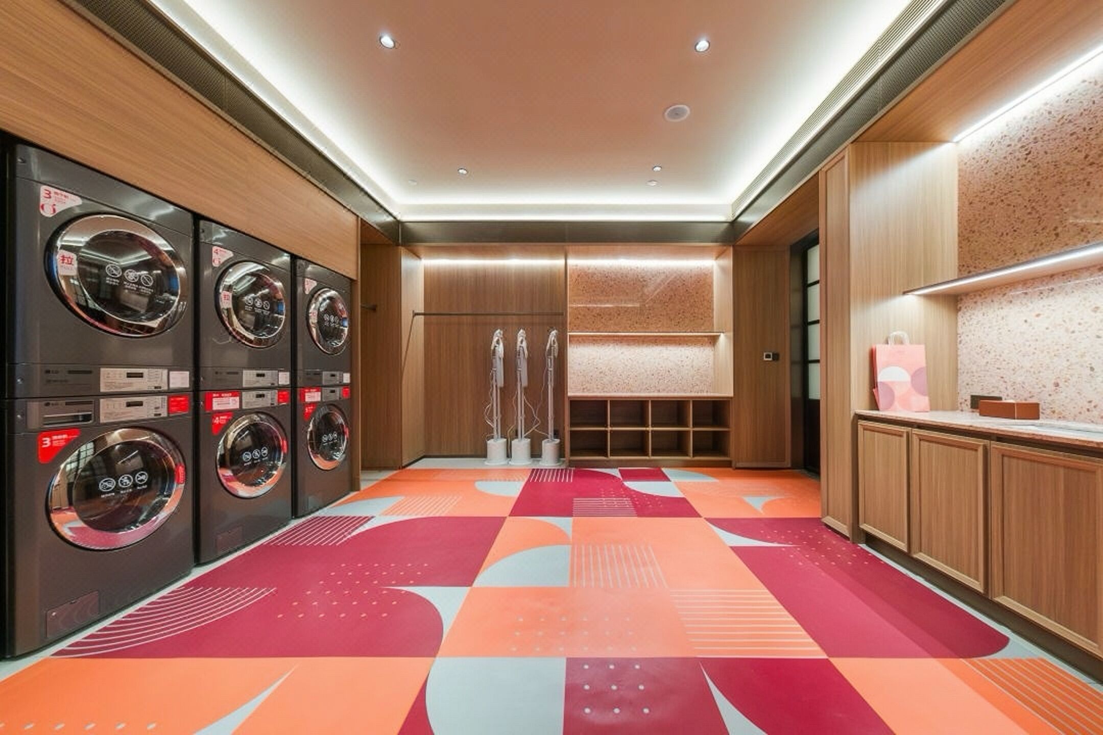 A modern laundry room with multiple washing machines, a patterned floor, and wooden cabinetry.