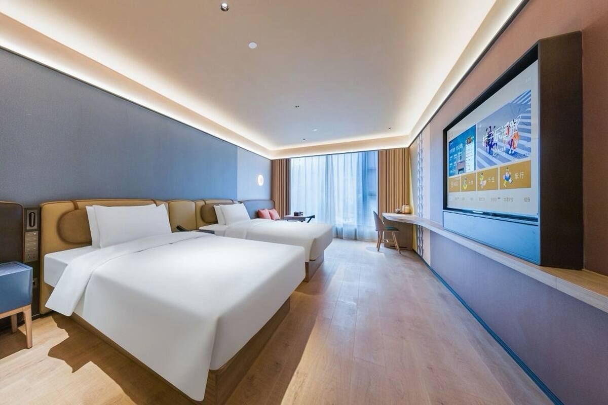 Habitación de hotel con dos camas, un escritorio y televisión en la pared.