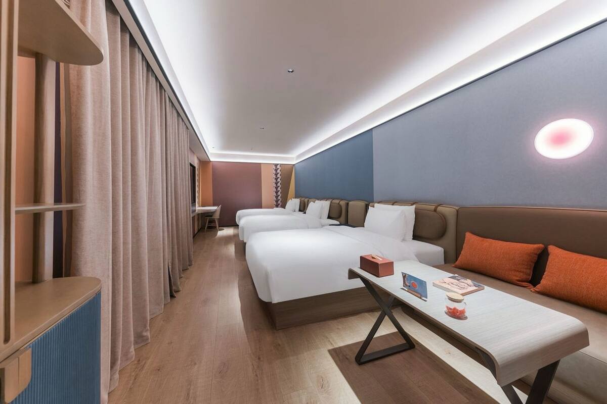 Una habitación de hotel moderna con dos camas, un sofá, una mesa y un ventanal grande.