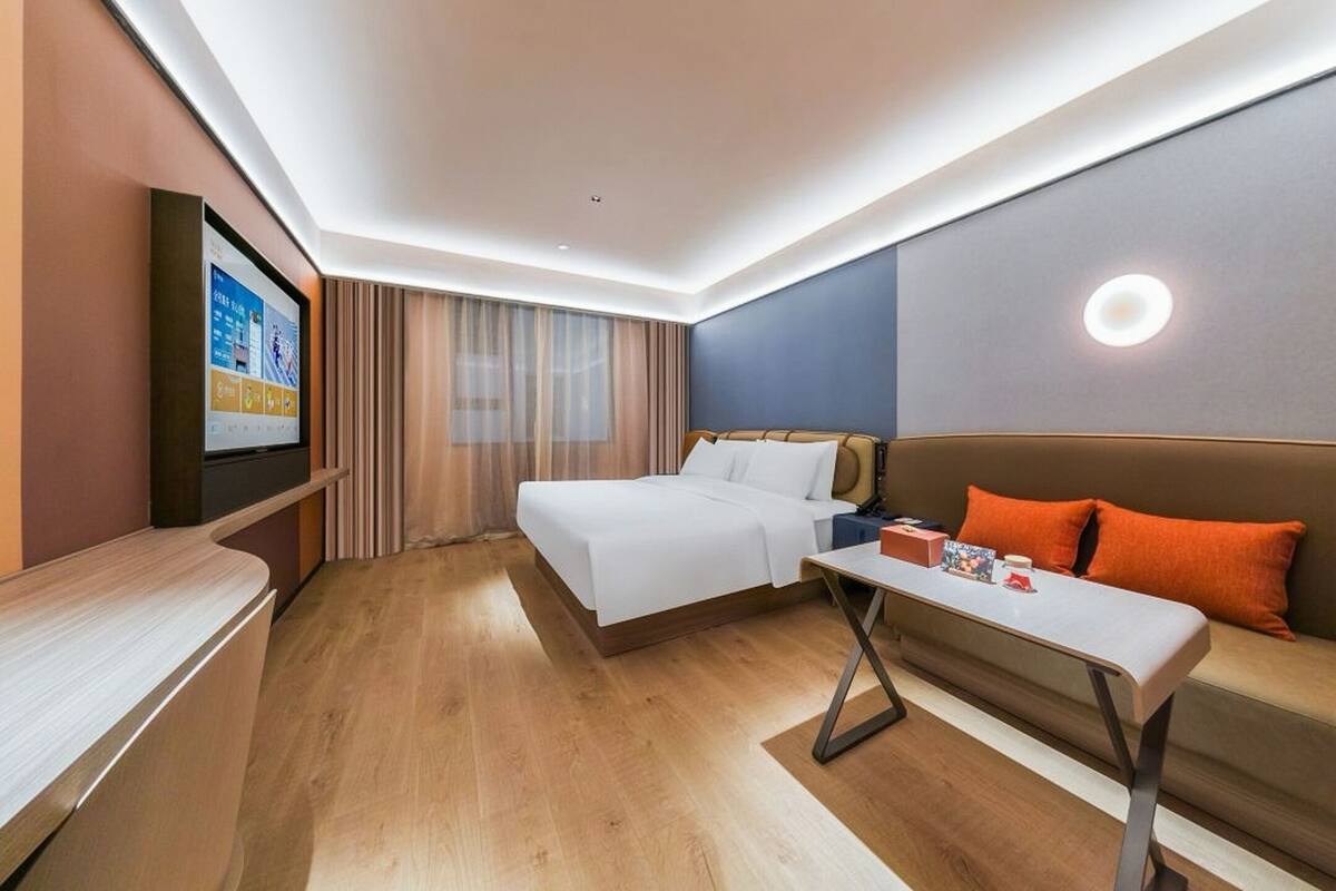 Habitación de hotel con cama, sofá, televisión en la pared y suelo de madera.