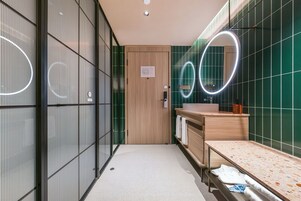 Un baño moderno con puerta de madera, un lavabo con espejo y paredes con azulejos verdes.