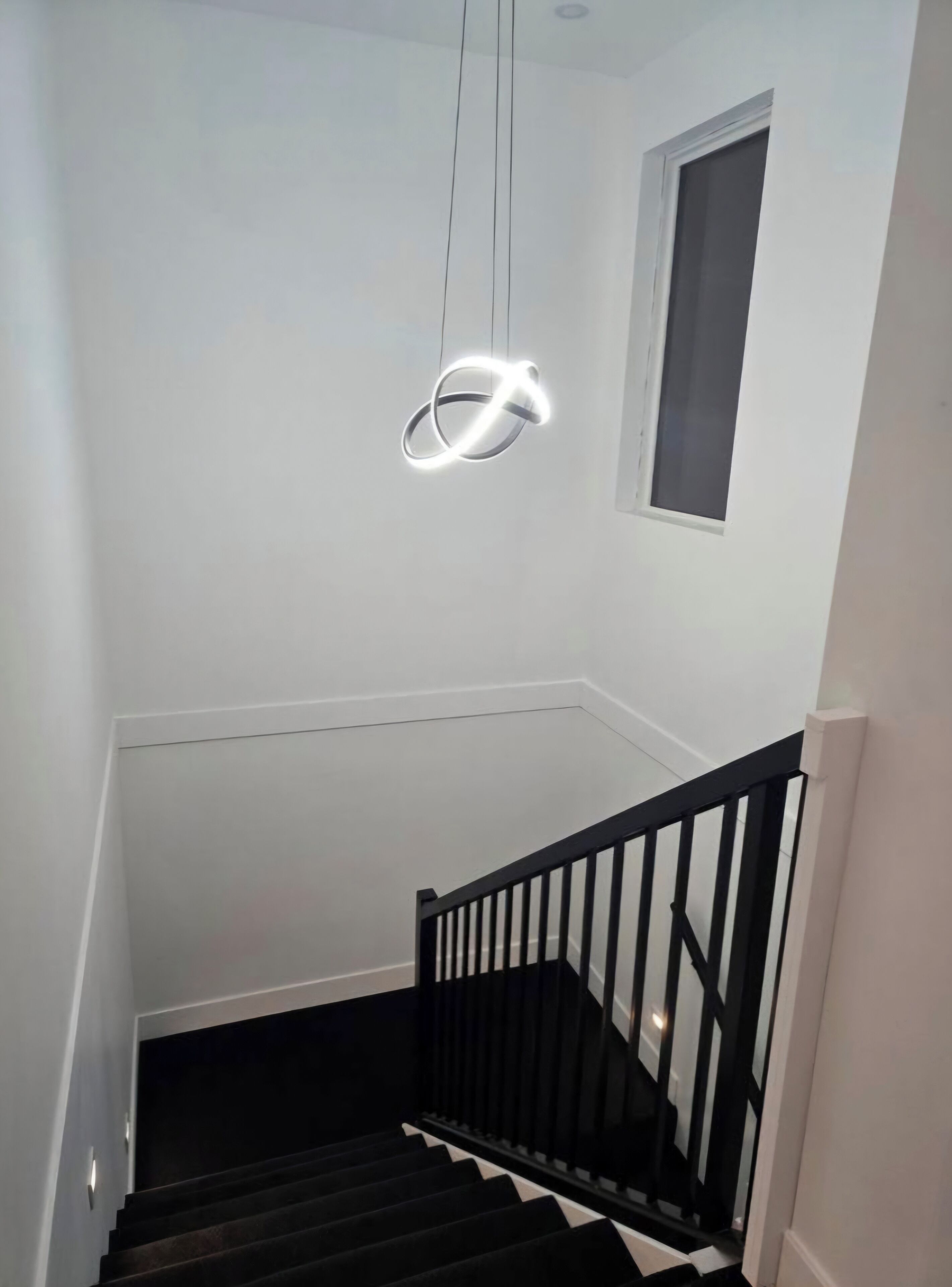Een trap met een zwarte leuning en een moderne lamp erboven.