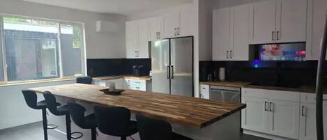 Une cuisine moderne avec des armoires blanches, un îlot central en bois doté de tabourets, un réfrigérateur en acier inoxydable et un téléviseur posé sur le plan de travail.
