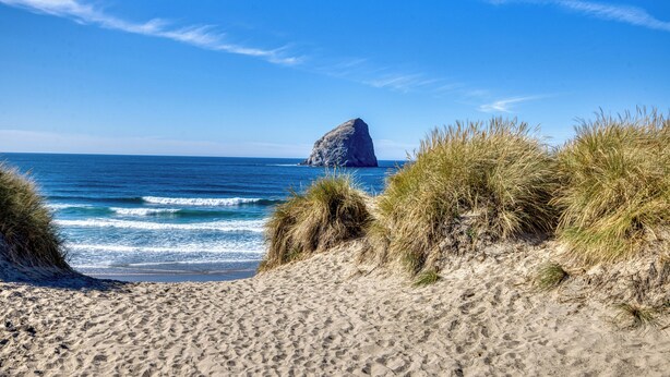 A beach with sand dunes, a rock formation in the distance, and the ocean. - Seahorse -Steps to beach, 3 bed, bikes, fireplace. (Pacific City)