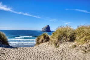 Une plage avec des dunes de sable, une formation rocheuse à l’horizon et l’océan.