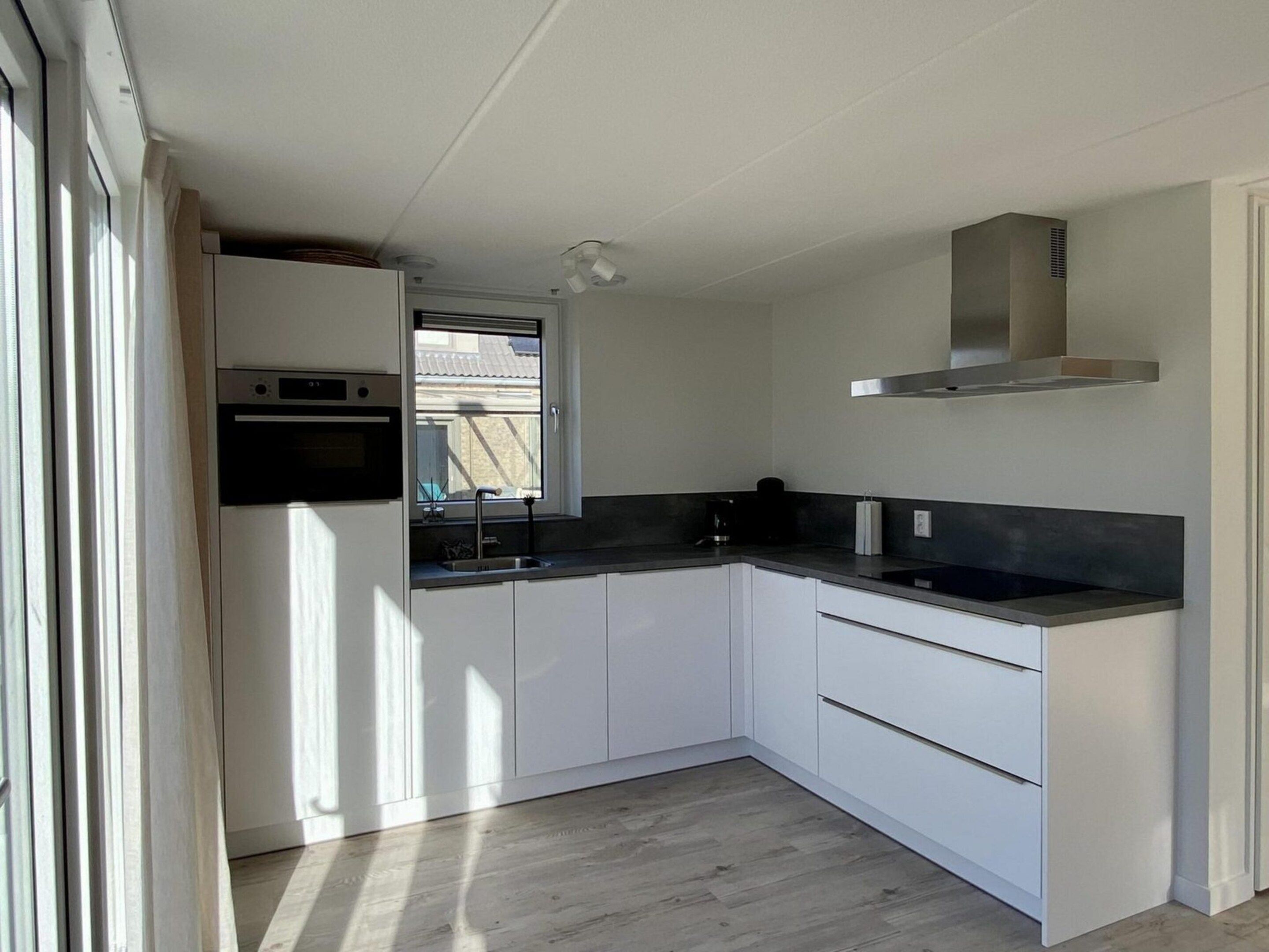 A modern kitchen with white cabinets, a black countertop, and a stainless steel range hood.