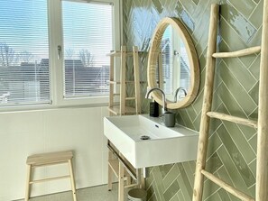 Une salle de bain avec un lavabo blanc, une échelle en bois et un miroir.