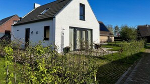 Une maison blanche d’un seul étage, avec un toit en pente, une cheminée bien visible et le chiffre « 72 » peint sur le mur.