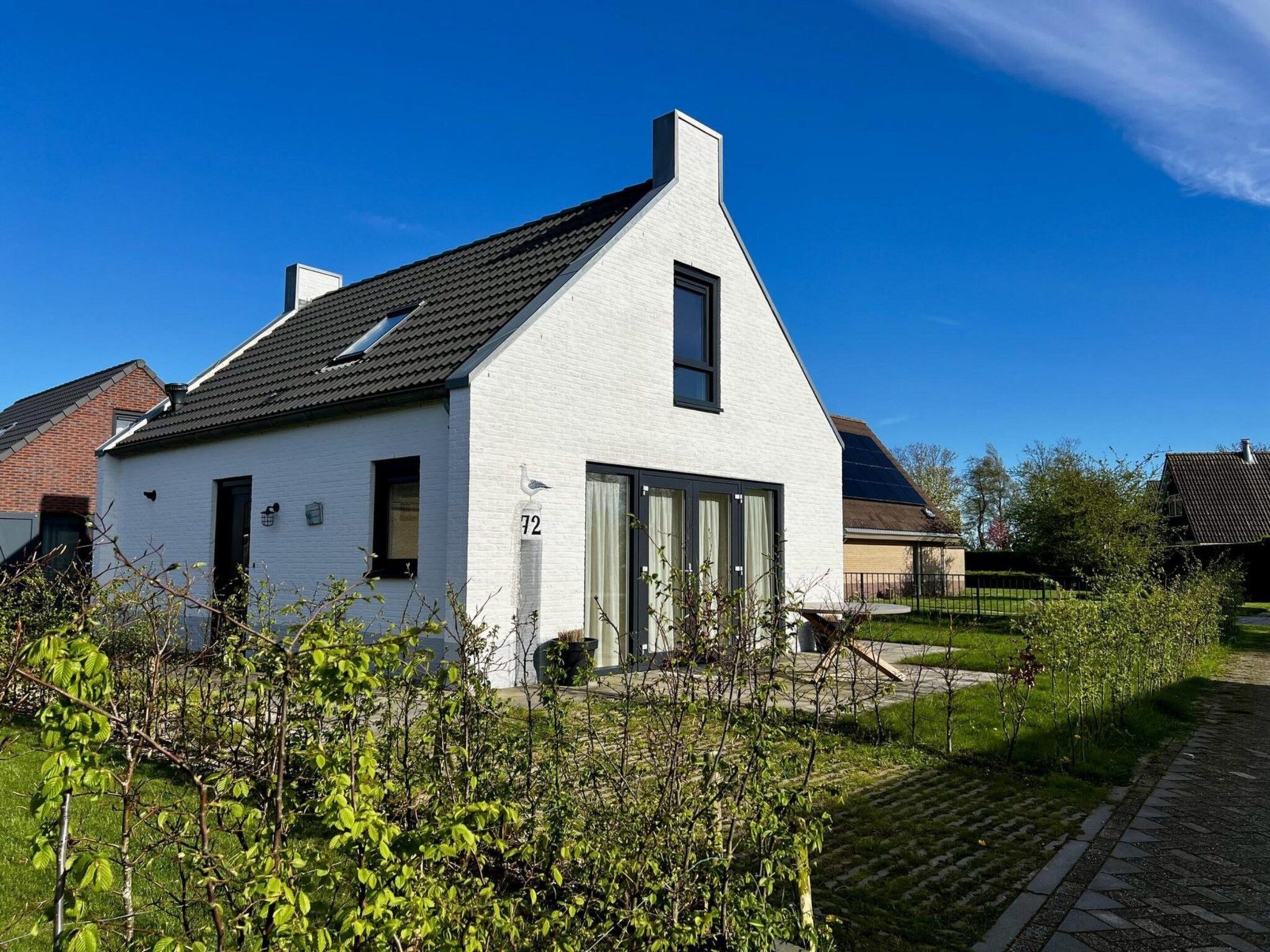 Ett envåningshus med vit fasad och ett sadeltak, ett tydligt synligt nummer ’72’ på framsidan och en liten trädgård framför huset.