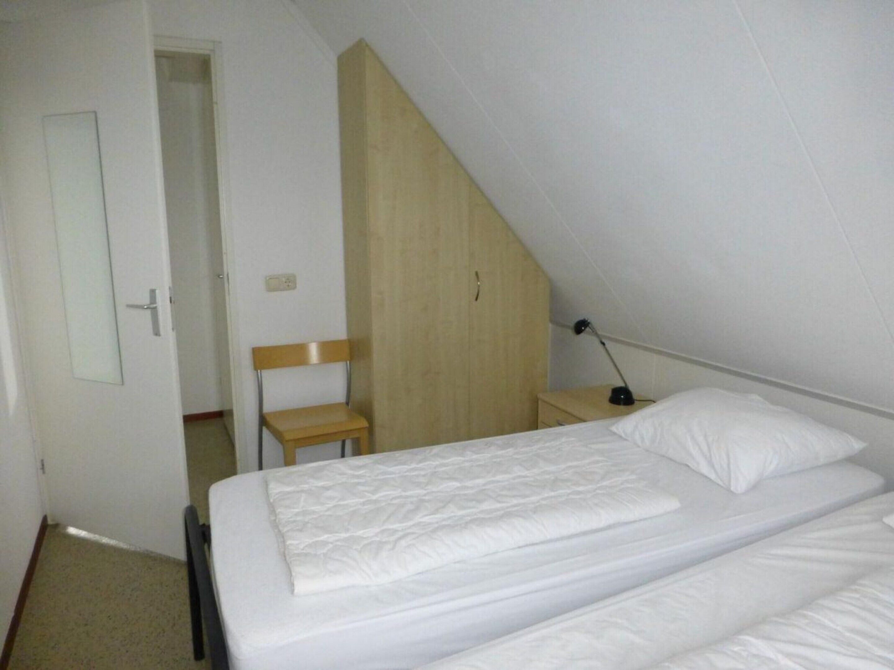 A small, simple room with a bed, a chair, and a desk.
