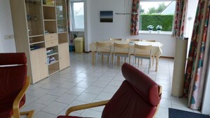A spacious room with a dining area, a red chair, a bookshelf, and a window with curtains. - Bungalow for 6 People, Near the Beach (Sint Maartensvlotbrug)