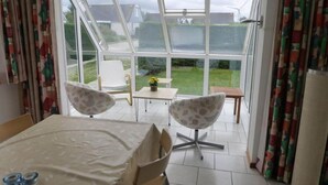 A room with a large glass door leading to a garden, a table with a tablecloth, two patterned chairs, and a small table with a vase of flowers. - Bungalow for 6 People, Near the Beach (Sint Maartensvlotbrug)
