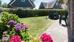 A courtyard with a lawn, a hedge, and two buildings with steep roofs. - Attractive Villa Close to Forest, Beach, sea (Sint Maartensvlotbrug)