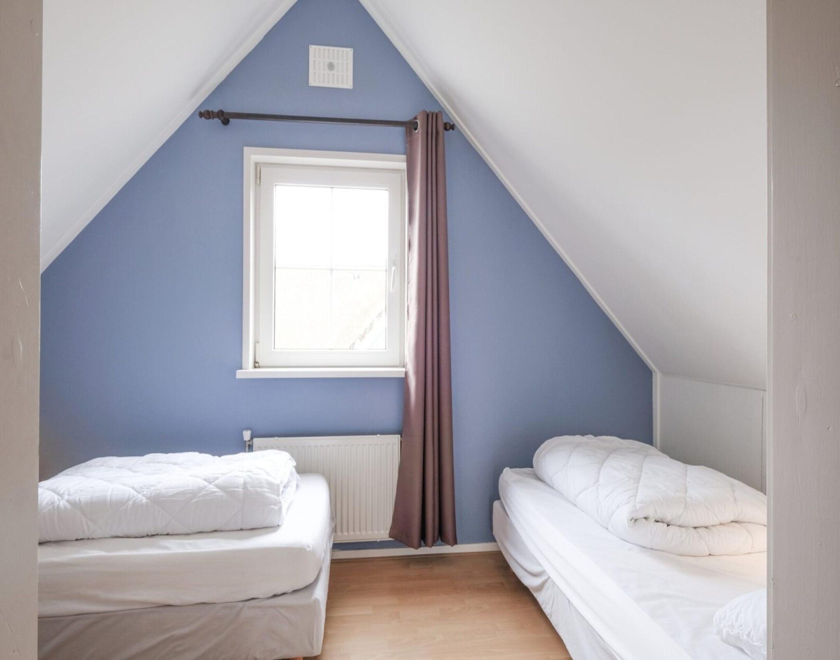 Een slaapkamer met twee bedden, een raam en een radiator.
