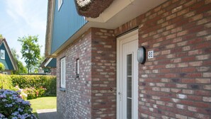 A brick exterior with a white door and mailbox, a bench, and a small garden with purple flowers. - Attractive Villa Close to Forest, Beach, sea (Sint Maartensvlotbrug)