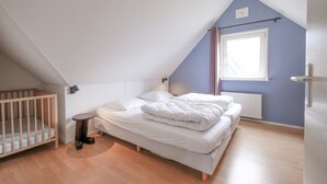 A bedroom with a sloped ceiling, a single bed, a small round table, a crib, and a window with curtains. - Attractive Villa Close to Forest, Beach, sea (Sint Maartensvlotbrug)