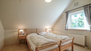 Ein Schlafzimmer mit einem hölzernen Bett, Nachttischen mit Lampen, einem Fenster mit Vorhängen und einer Heizung.