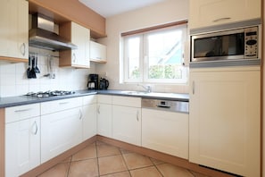 Une cuisine avec des meubles blancs, une cuisinière à gaz, une machine à café et une fenêtre donnant sur un beau paysage.