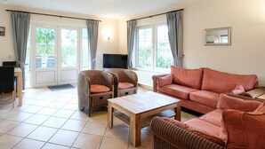 Ein Wohnzimmer mit einer Couch, zwei Sesseln, einem Couchtisch, einem Fernseher und einem Fenster mit Vorhängen.