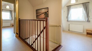Ein Korridor mit einer Holztreppe, einem Heizkörper, einem Fenster mit Vorhängen und einem Gemälde an der Wand.