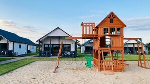 Un parque infantil con un columpio de madera y una estructura para escalar en una zona residencial con casas.