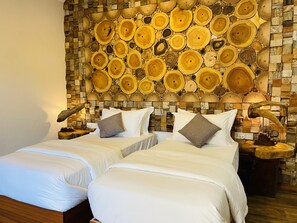 Camera d'albergo con due letti, una parete in legno a tronchi e un comodino con una lampada.