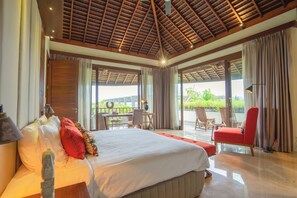 A spacious bedroom with a large bed, a desk, and a chair, and a balcony with a view of greenery. - OMEKAI Cemagi by Nakula (Cemagi)